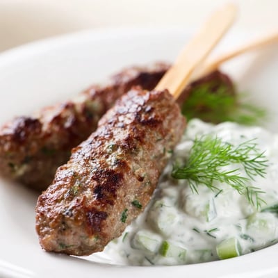 Golden-brown Beef Kofta Kebabs resting on a platter, paired with a creamy cucumber yogurt dip for a savory bite.