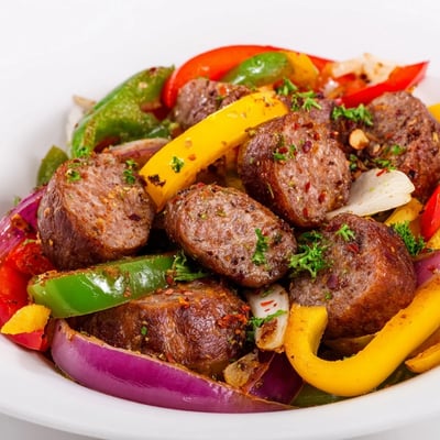 Bright red, yellow, and green peppers mingle with seared spicy beef sausage in a cast-iron skillet, perfect for serving over rice.