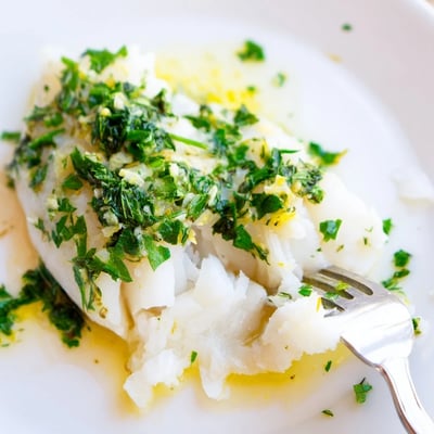 Golden Baked Cod with Lemon Herb Butter topped with fresh herbs and lemon zest flakes easily on a white plate. 