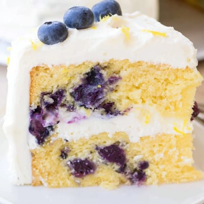 Slice of Lemon Blueberry Cake with Cream Cheese Frosting revealing tender crumb with lemon zest and plump blueberries, served on a white plate.
