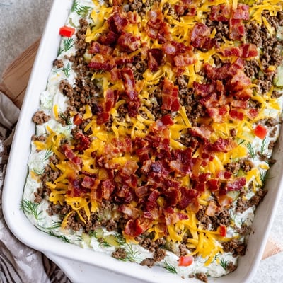 Serving suggestion for Low Carb Bacon Cheeseburger Casserole with a scoop on a white plate, garnished with fresh green onions and extra pickles.