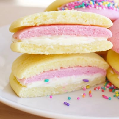 A close-up of pastel sugar cookie sandwiches showing creamy vanilla buttercream filling.