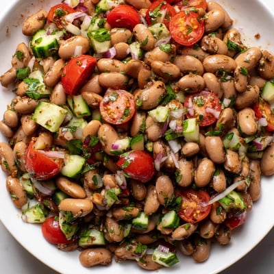 Creamy pinto beans mixed with diced cucumbers tomatoes and cilantro in bowl