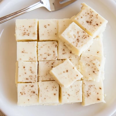Slices of Eggnog Fudge cooling in refrigerator, speckled with warm spices